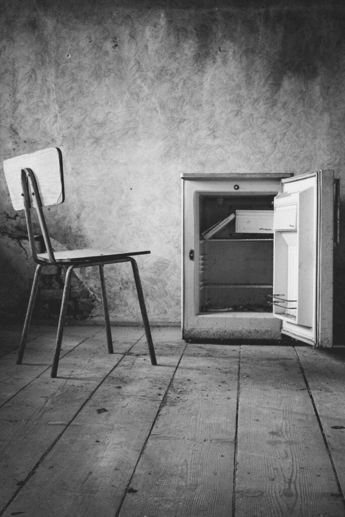 Verhuur Black and white photo of an abandoned room with a chair and open mini fridge.